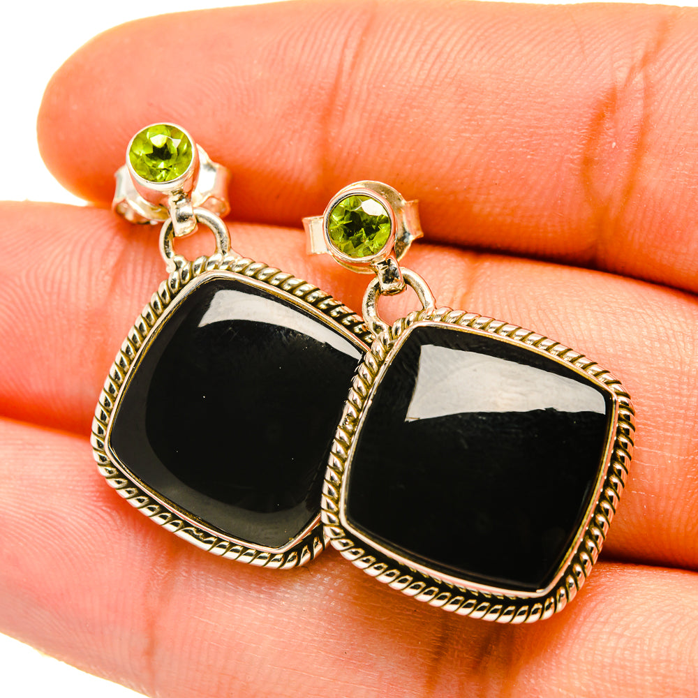Gold drop earrings close-up with black square stones, rope border, and peridot-green studs