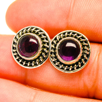 Close-up of round amethyst stud earrings with gold-tone filigree bezel on silver