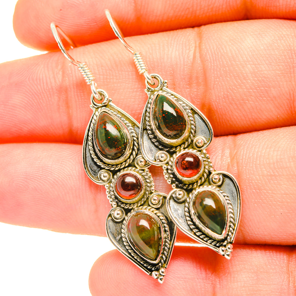 Gold-tone drop earrings with green teardrop stones and red accents, close-up