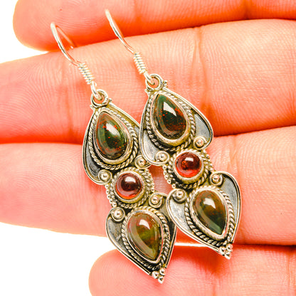 Gold-tone drop earrings with green teardrop stones and red accents, close-up