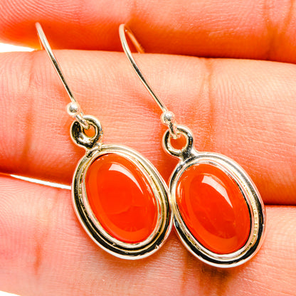 Close-up of orange oval gemstone drop earrings with silver bezel and French hooks