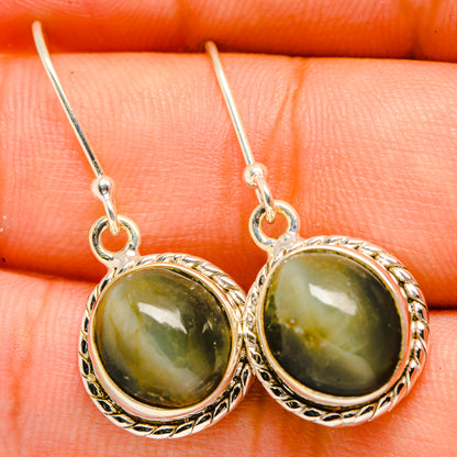 Cat's eye earrings close-up: green cabochon rounds in silver ornate bezels, hook
