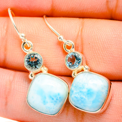 Close-up of blue gemstone drop earrings with oval larimar cabochons and round topaz settings