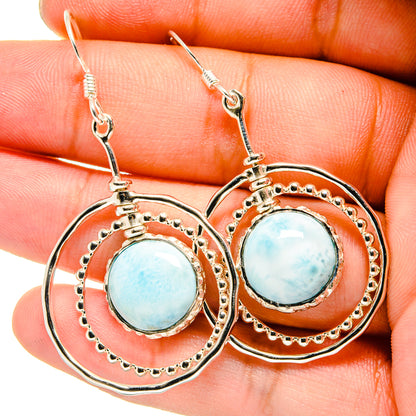 Close-up of sterling silver Larimar drop earrings, blue round stone in scalloped frame