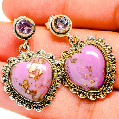Close-up of heart-shaped pink stone drop earrings with purple crystal studs and ornate gold-tone settings