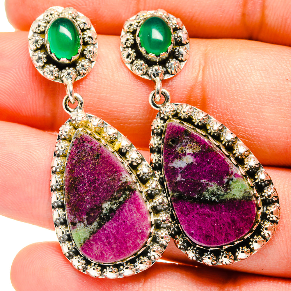 Close-up of teardrop earrings: green oval stud and purple teardrop dangle in silver setting