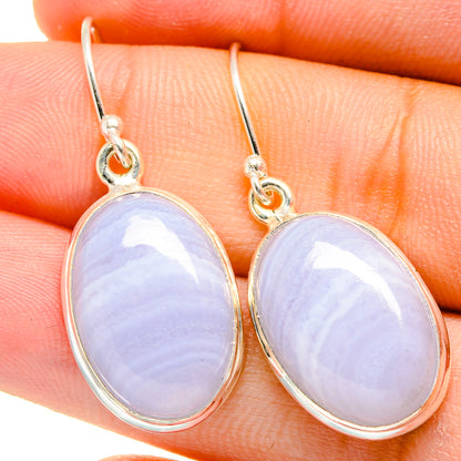 Oval blue lace agate drop earrings with silver hooks, close-up on finger