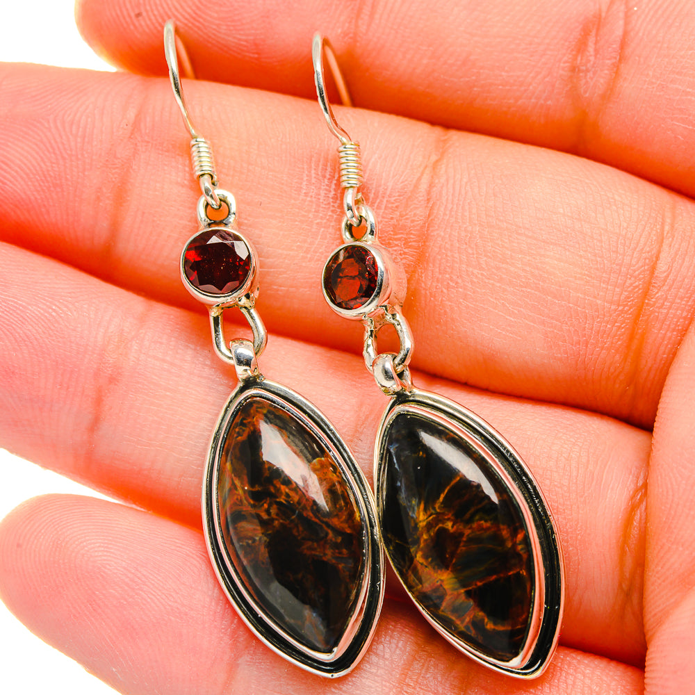 Close-up of sterling silver drop earrings: round red stone tops, oval pietersite drops