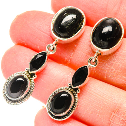 Oval black onyx dangle earrings with silver halo bezels, dangling from ear wires