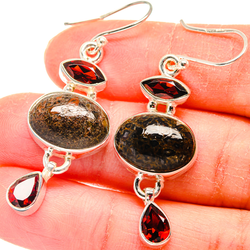 Close-up of garnet and dinosaur-bone drop earrings with teardrop red stones, silver hooks