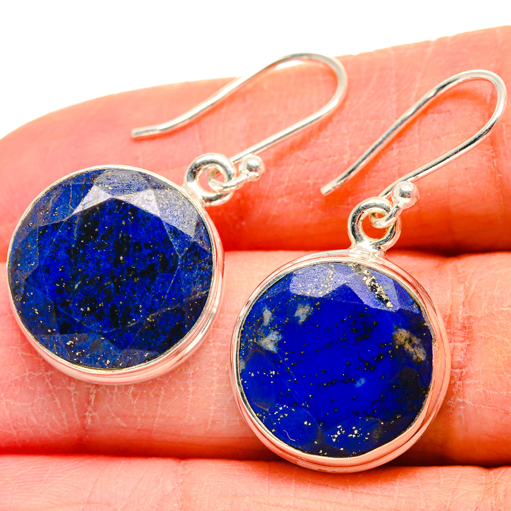 Sterling silver lapis lazuli round drop earrings on finger, blue stone with speckled flecks.
