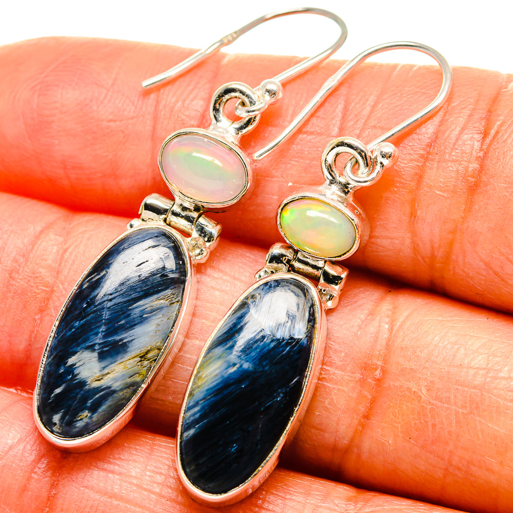 Sterling silver drop earrings on skin: blue oval stone with iridescent opal center.