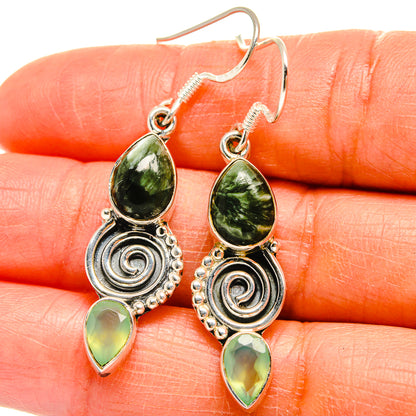 Close-up of green drop earrings with teardrop gems and silver swirl medallions on hooks