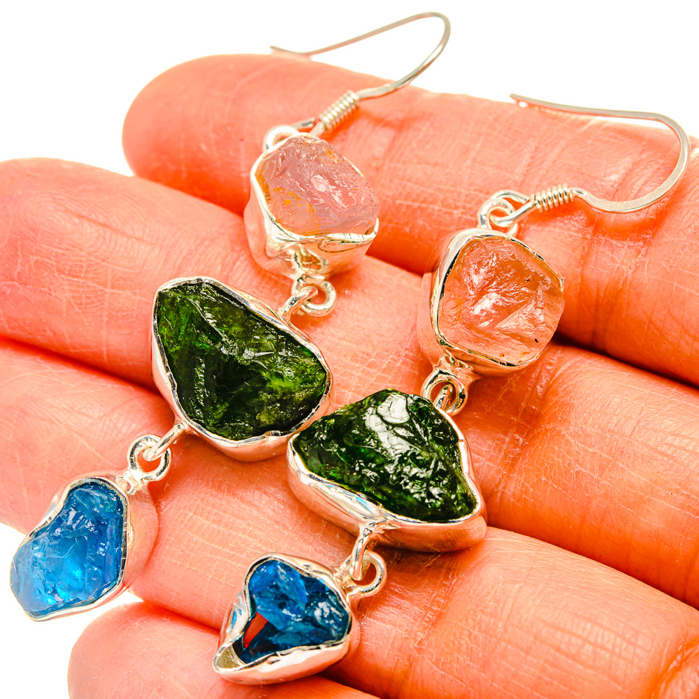 Close-up dangling sterling silver earrings with rough orange, green, blue stones
