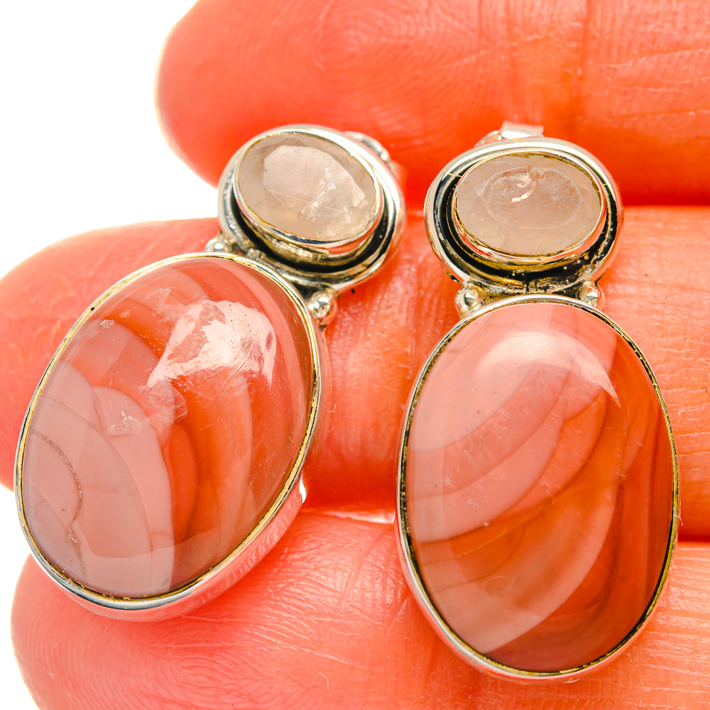 Close-up of oval pink gemstone earrings in gold-tone bezels on silver settings
