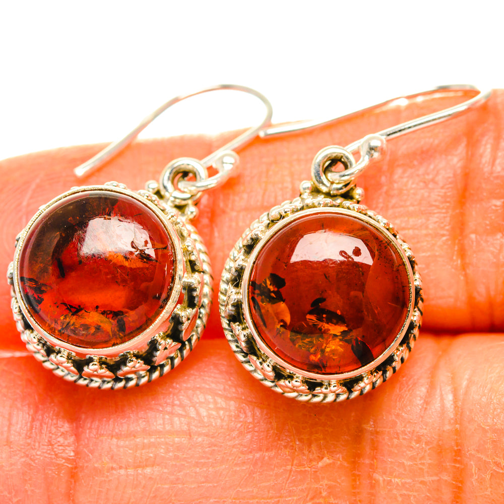 Round amber cabochon earrings with ornate silver frame and fishhook, red-orange glow