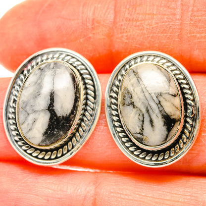 Close-up of oval pinolith jasper stud earrings, white stone with dark veins, silver bezel.