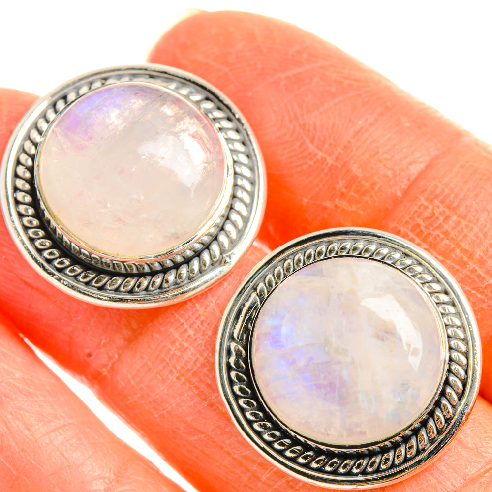 Round opalescent moonstone stud earrings with ornate sterling-silver bezel, close-up