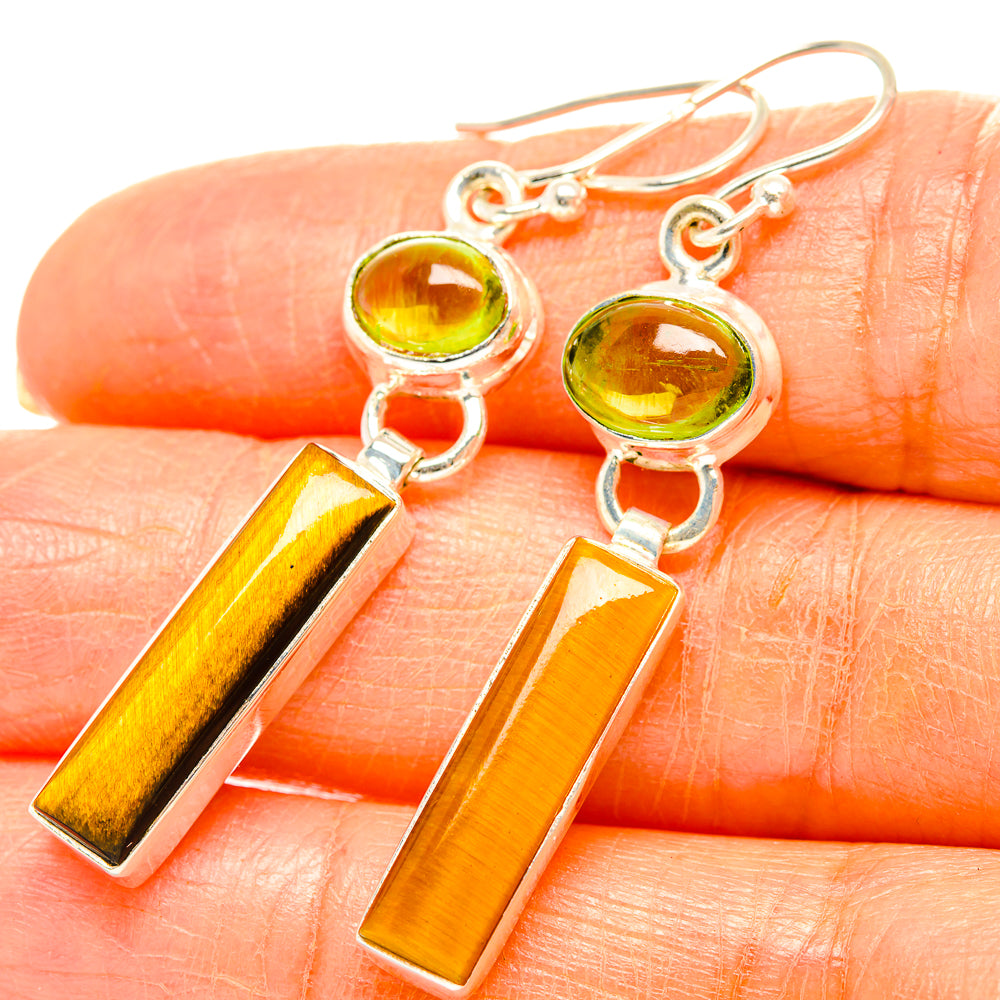 Close-up of peridot and tiger eye drop earrings with amber rectangular stones on fingers