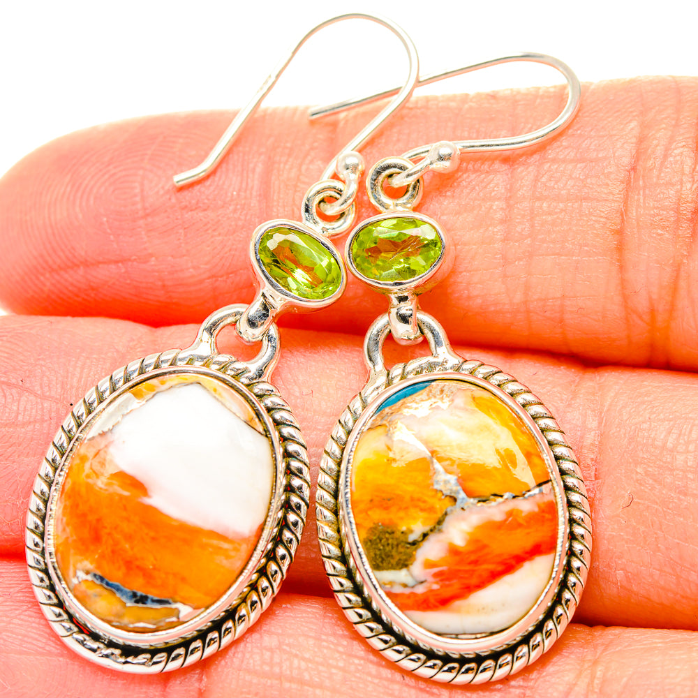 Close-up of sterling silver drop earrings with green peridot tops and oval spiny oyster stones
