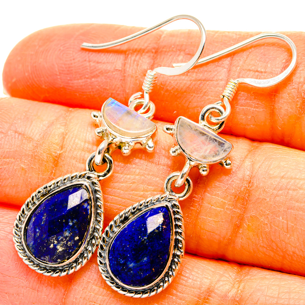 Close-up of silver dangling earrings with blue lapis teardrop stones and pale moonstone caps