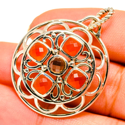 Close-up round gemstone pendant with orange stones and dark center, silver filigree loop