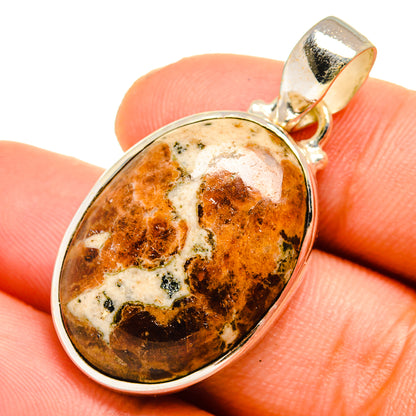 Oval muscovite pendant with amber orange marbled stone, shown on fingertip
