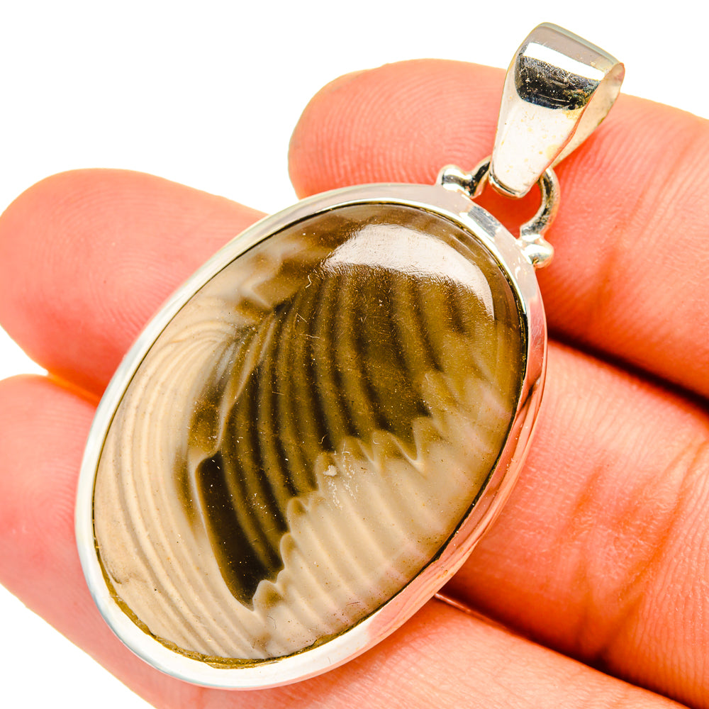 Oval jasper pendant held in hand: silver bezel with brown/cream striped stone, gold bail