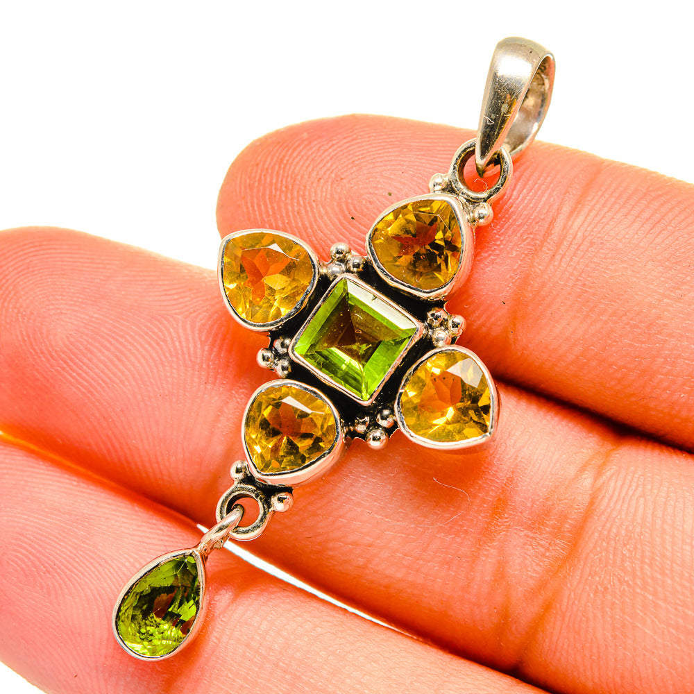 Sterling silver cross pendant with green and yellow faceted stones, on finger