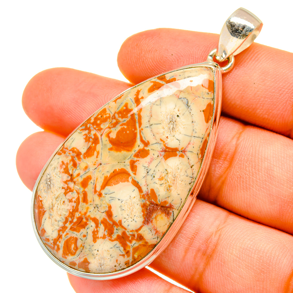Teardrop poppy jasper pendant held in hand, silver bail and orange veined stone