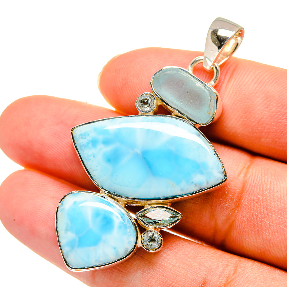 Blue cabochon gemstone pendant with small round accents and silver bail, in hand