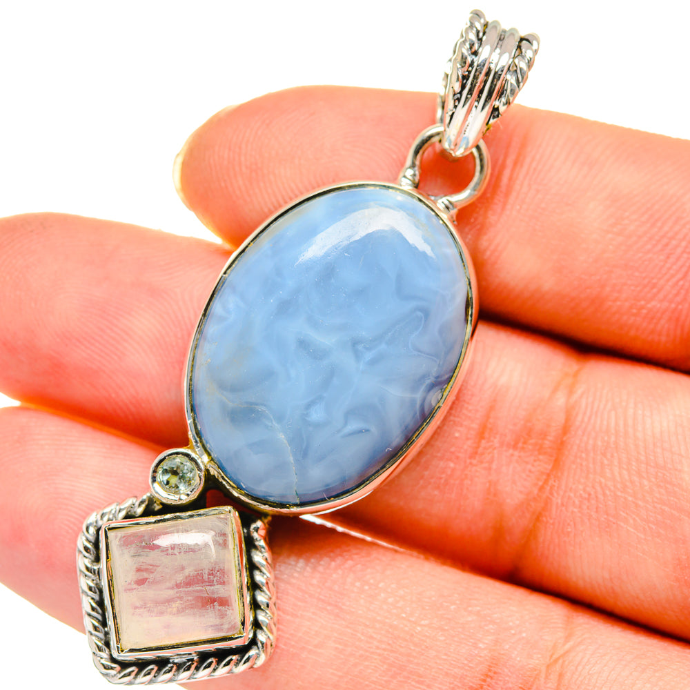 Sterling silver pendant with oval light-blue gemstone and square accent, held in hand