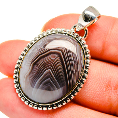 Oval agate pendant closeup, striped brown-and-cream cabochon in beaded silver frame