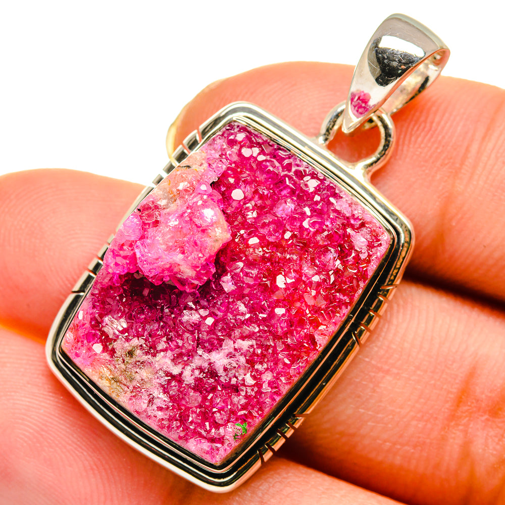 Pink druzy agate pendant on finger with silver-tone bezel and loop bail, rectangular frame