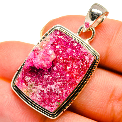 Pink druzy agate pendant on finger with silver-tone bezel and loop bail, rectangular frame