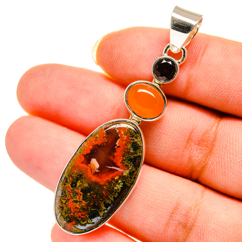 Silver pendant close-up with large oval speckled stone, orange round stone, and dark garnet