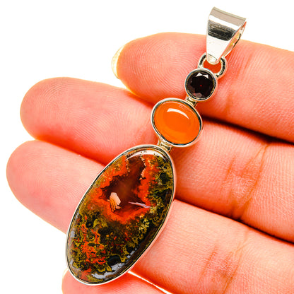 Silver pendant close-up with large oval speckled stone, orange round stone, and dark garnet