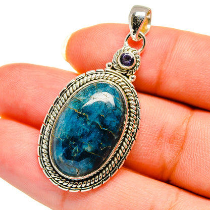 Oval blue gemstone pendant with ornate silver bezel and small purple stone accent bail.