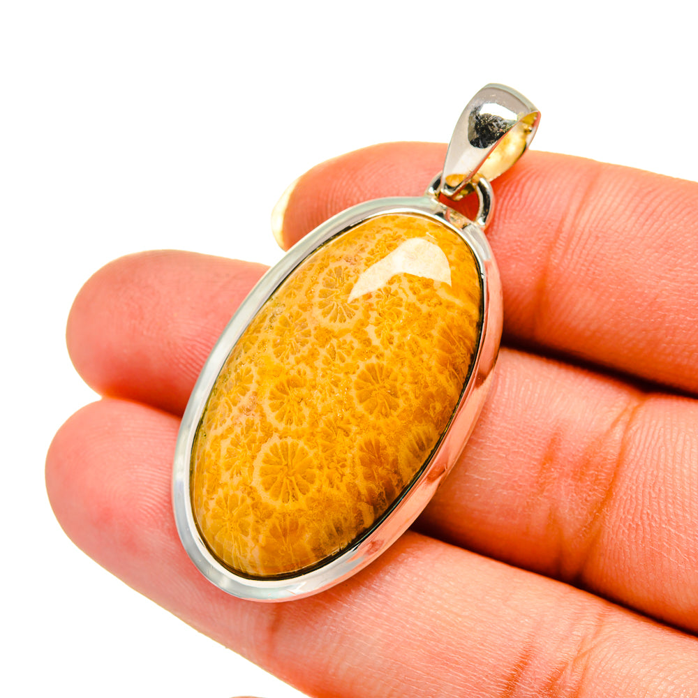 Oval orange coral pendant shown held in hand, sterling silver oval bezel