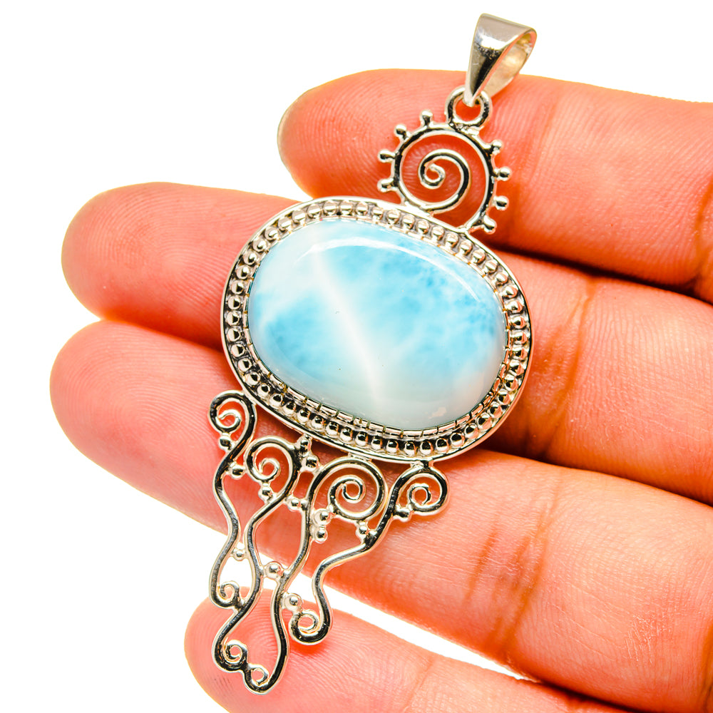 Sterling silver pendant with oval blue stone held in fingers