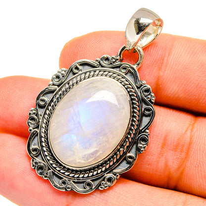 Oval moonstone pendant in silver with ornate bezel and hanging loop on top.
