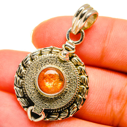 Round silver pendant with ornate border and glowing orange sunstone cabochon center