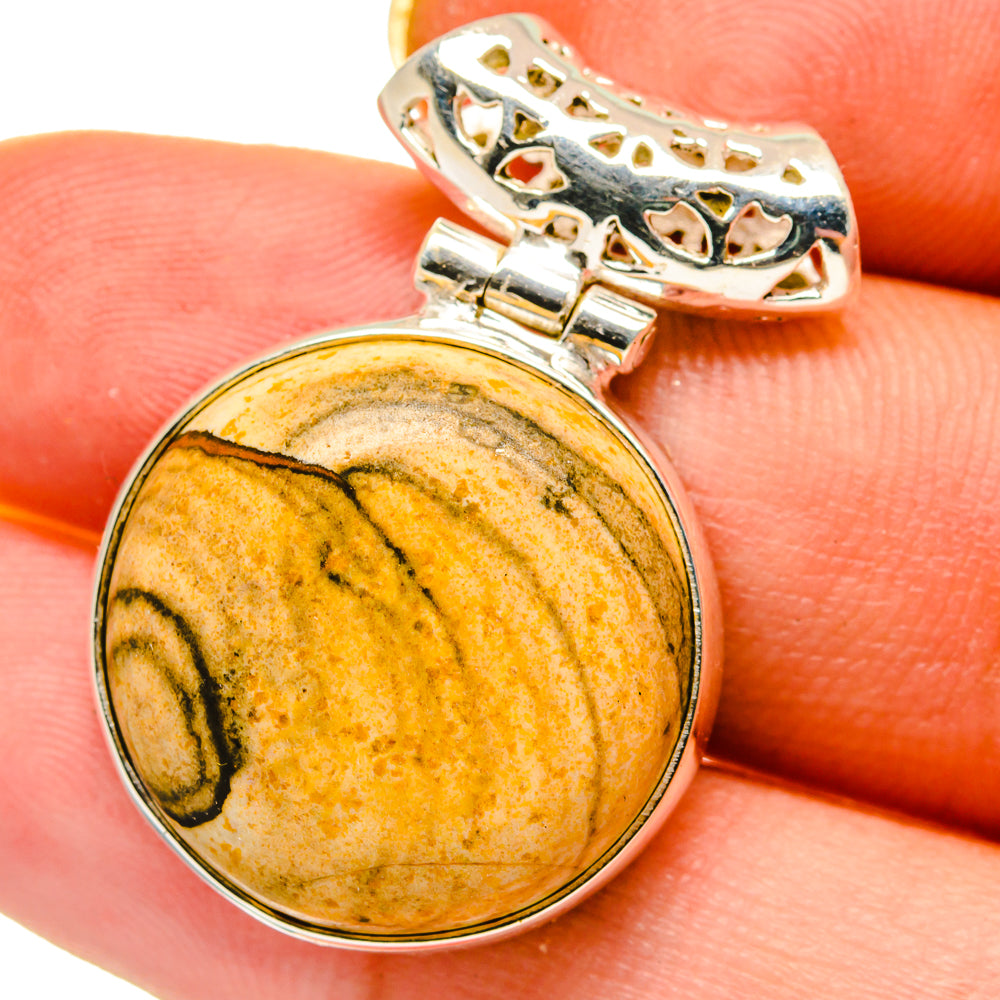 Round picture jasper cabochon pendant in sterling silver, held against a fingertip