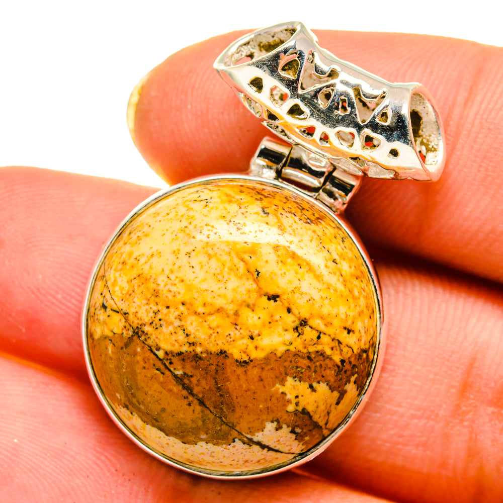 Round picture jasper pendant on finger with ornate silver bail and bezel