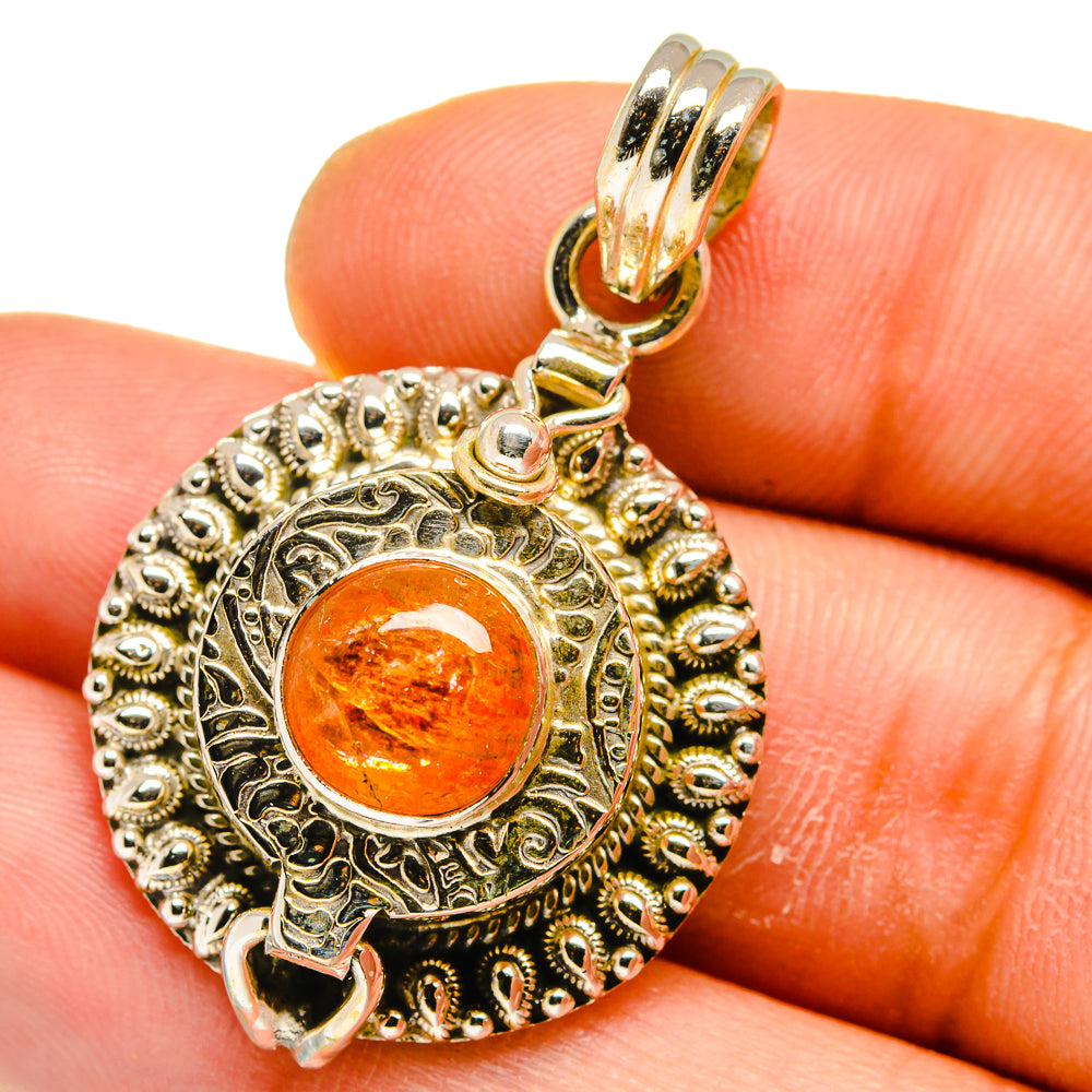 Ornate round poison pendant with orange sunstone cabochon in gold and silver-tone frame