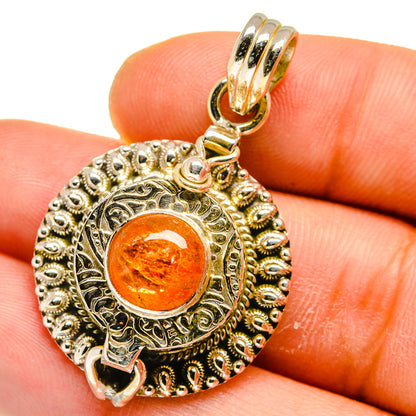 Ornate round poison pendant with orange sunstone cabochon in gold and silver-tone frame