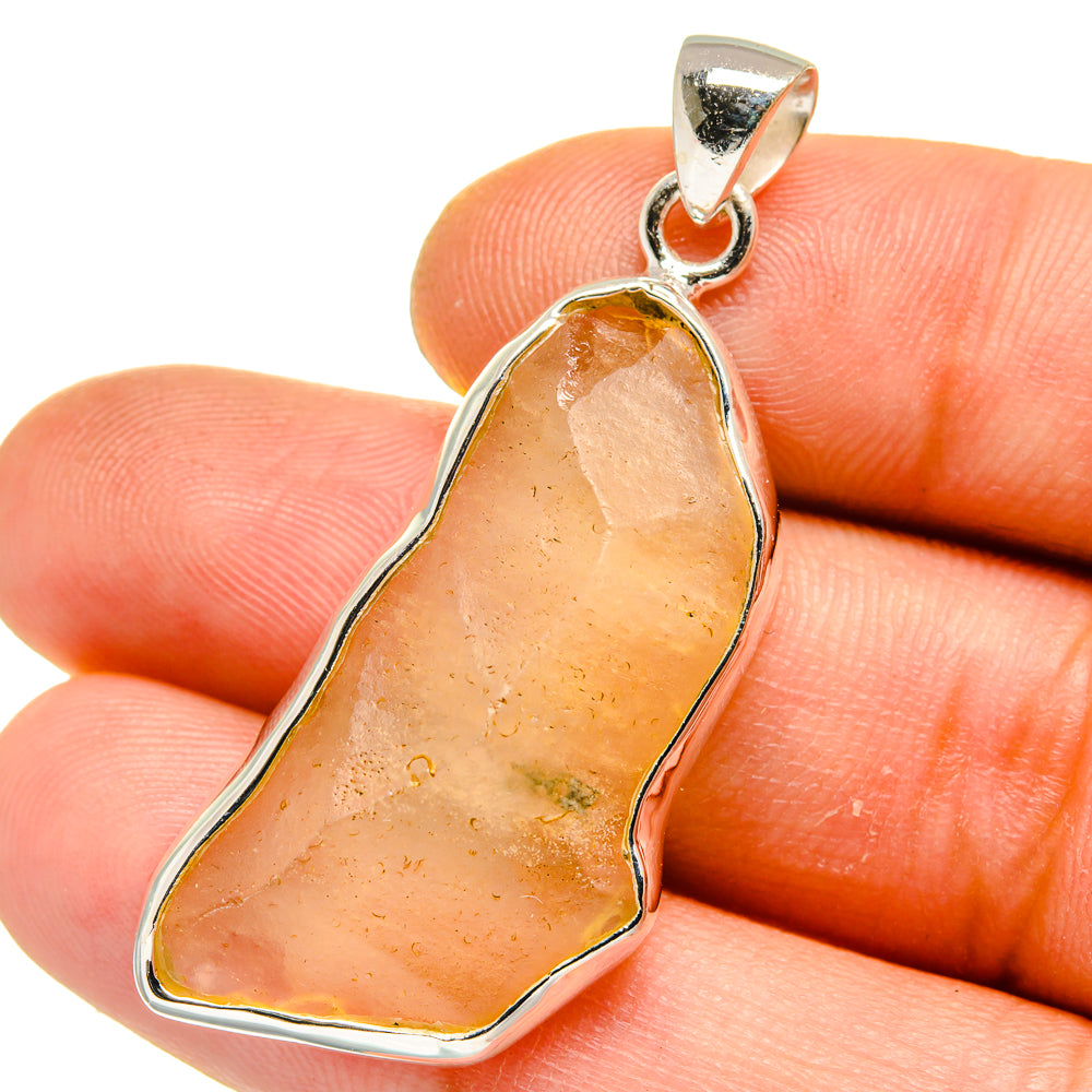 Amber glass pendant in 925 sterling silver bezel, teardrop shape, on fingertip