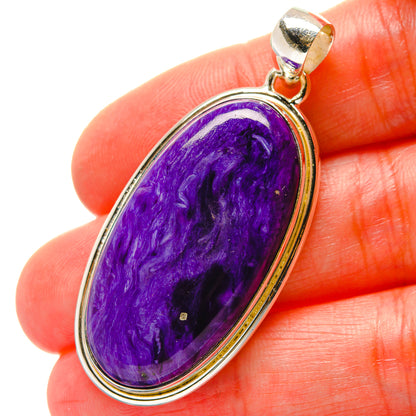 Oval purple charoite pendant in 925 sterling silver bezel, held on fingertip