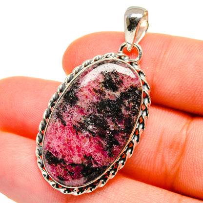 Oval rhodonite pendant with textured sterling silver frame and top bail on finger
