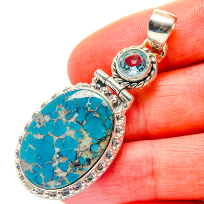 Oval turquoise cabochon pendant with ornate silver setting and small blue stone
